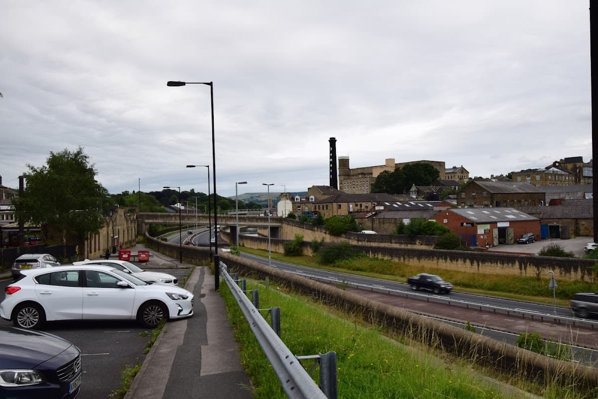 Pay & Display car park with parked cars, green grass, and a view of buildings and a road in Bingley, Yorkshire.