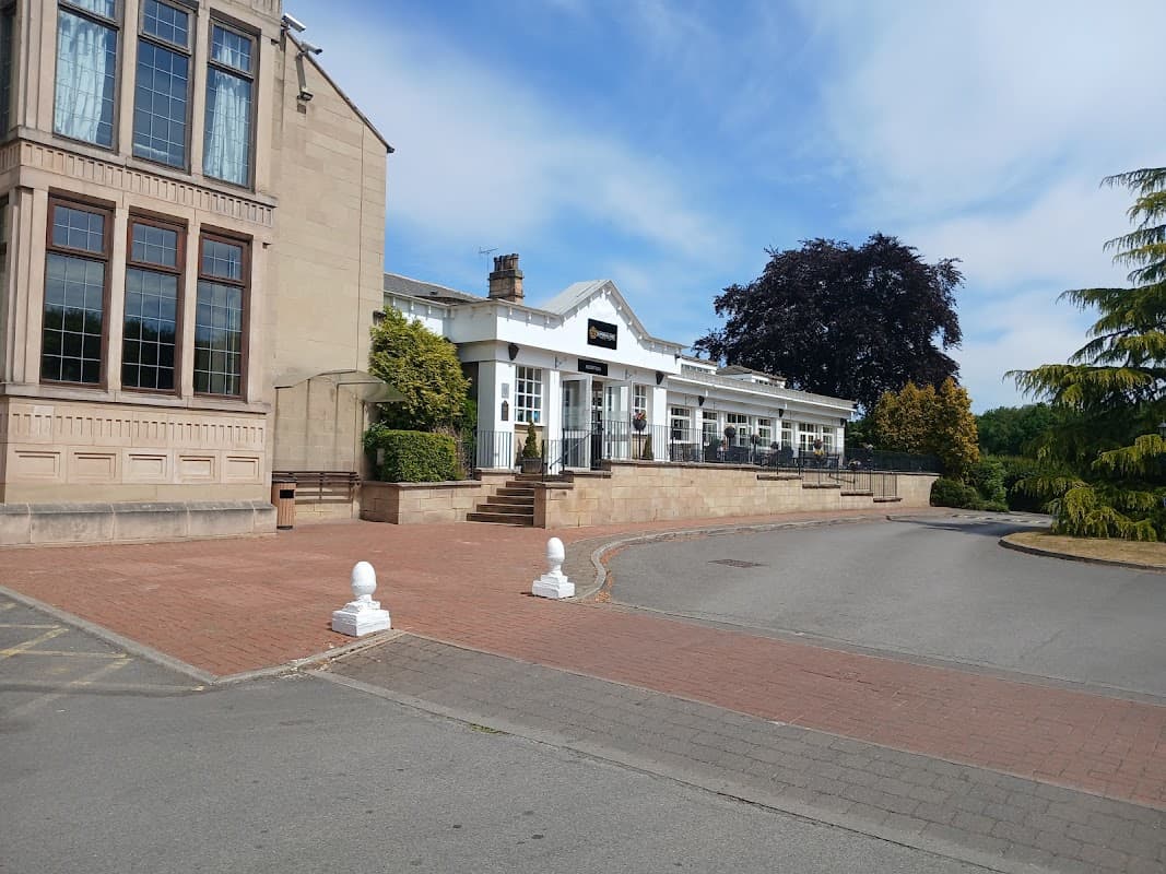 Gomersal Park Hotel features a stone facade, outdoor seating area, and landscaped greenery against a clear blue sky.