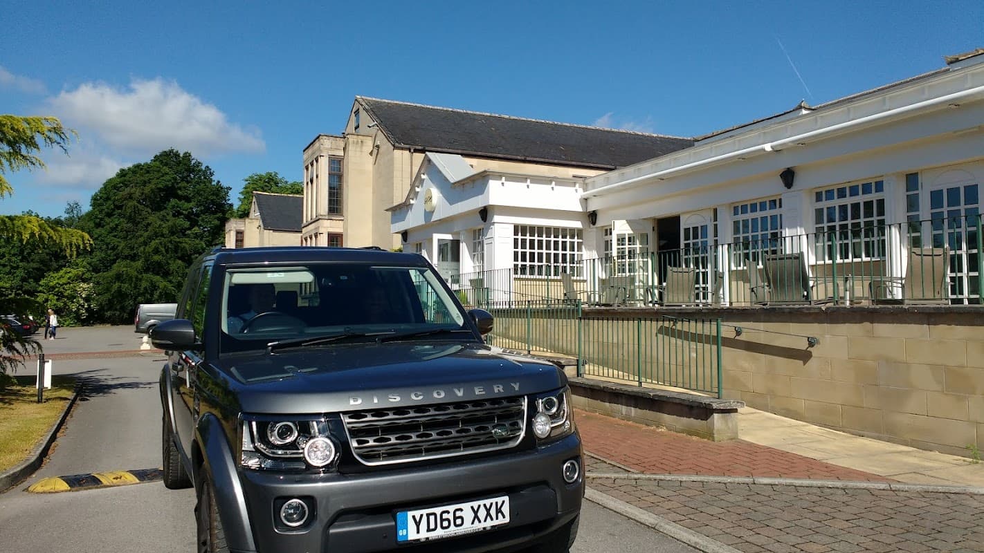 Modern hotel building with large windows, green trees, and a parked black Discovery vehicle in front.