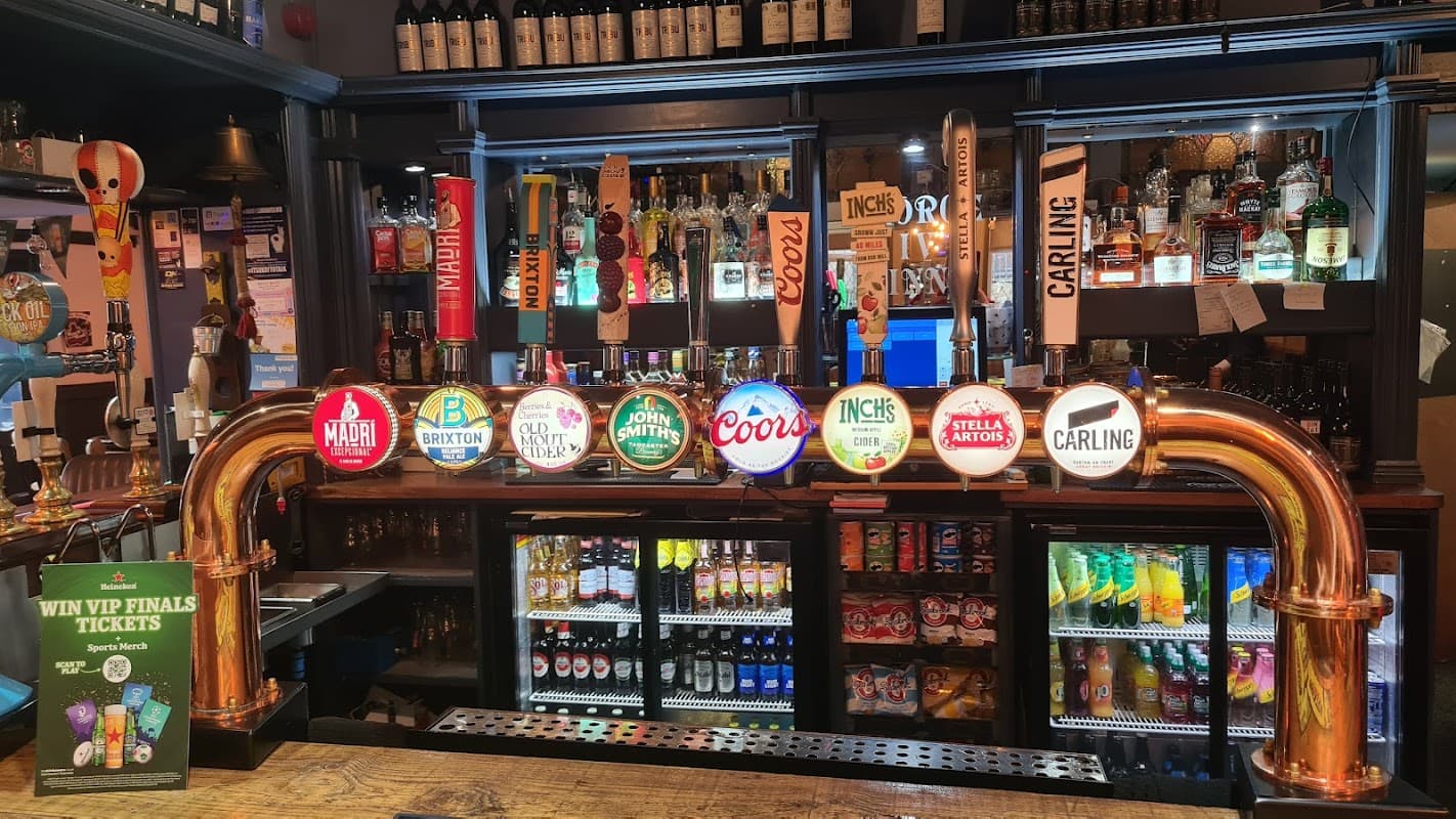 Bar counter featuring a variety of beer taps, colorful beer signs, and shelves stocked with bottles behind the bar.