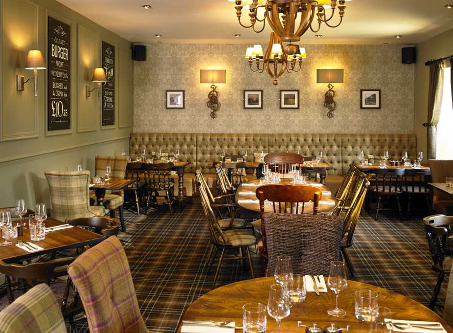 Elegant restaurant interior featuring wooden tables, upholstered seating, and decorative wall sconces in a cozy atmosphere.