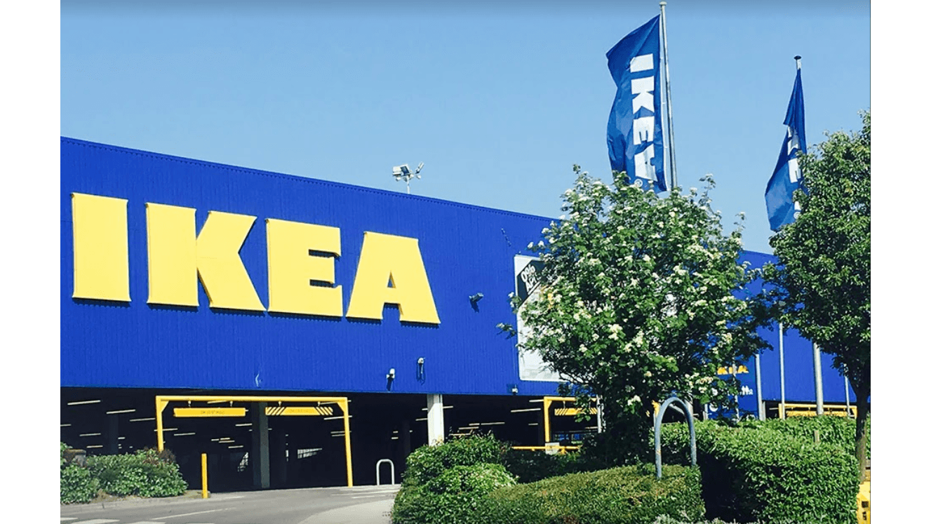 Bright blue IKEA building with large yellow signage, surrounded by green shrubs and flags waving in the breeze.