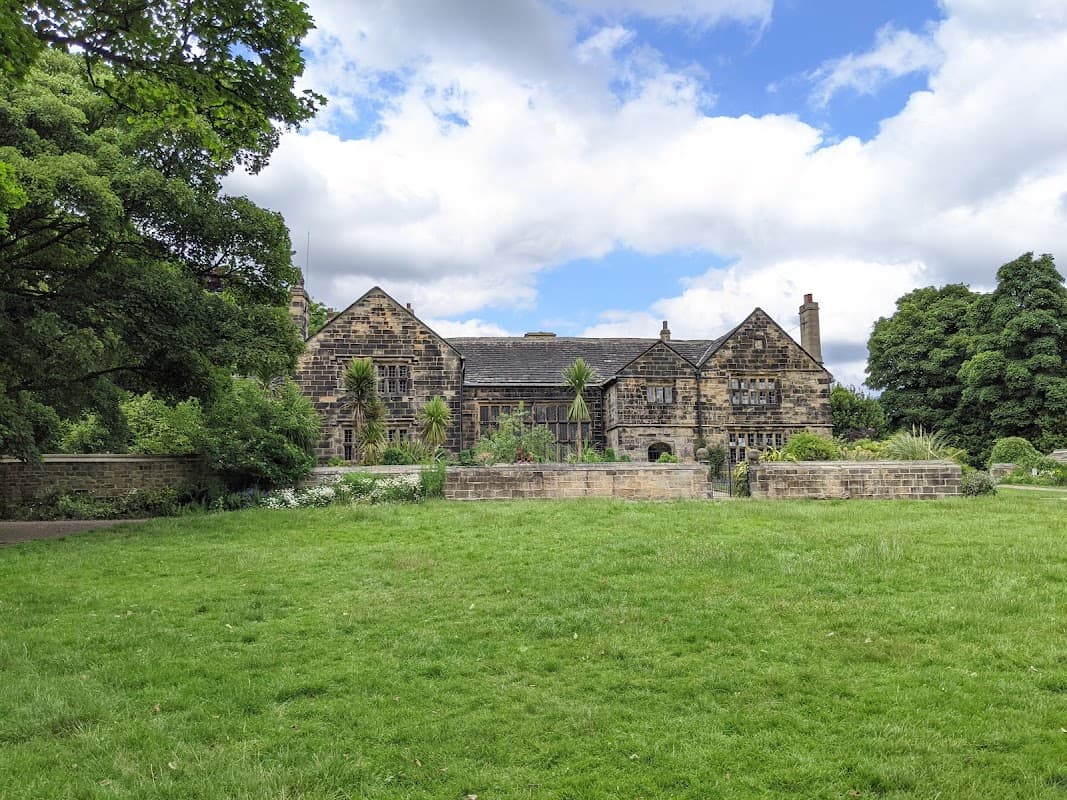 Historic stone building surrounded by lush greenery and trees under a partly cloudy sky.