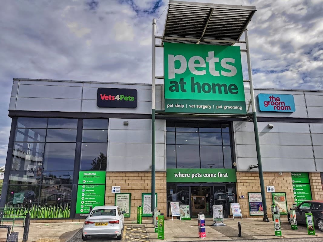 Large pet shop building with green signage, featuring "Pets at Home," "Vets4Pets," and "the groom room." Cars parked outside.