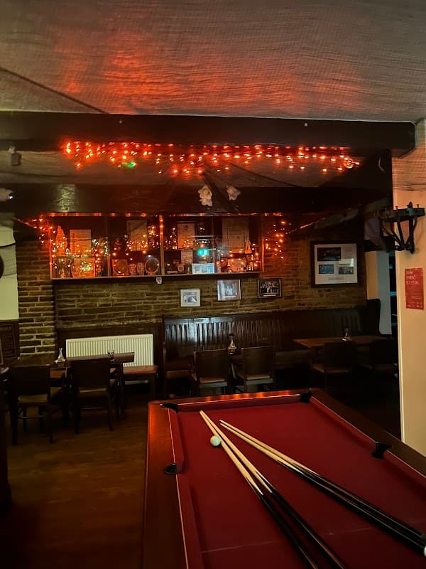 Cozy bar interior with a pool table, warm lighting, and rustic brick walls adorned with framed pictures.
