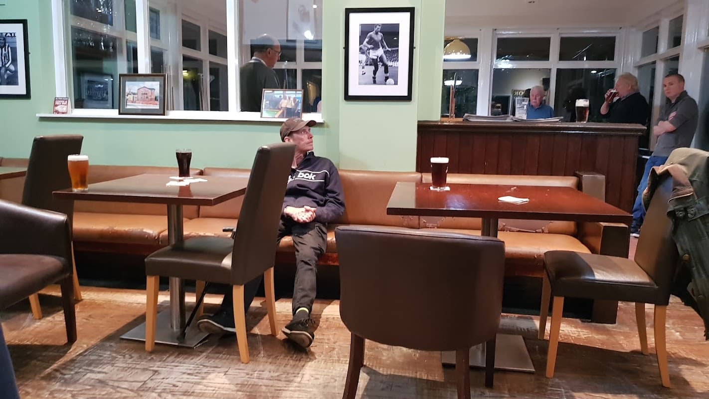 Cozy restaurant interior with wooden tables, leather seating, and patrons enjoying drinks in a relaxed atmosphere.