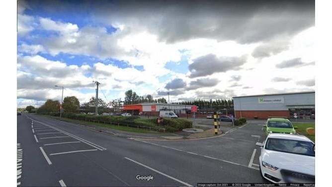 Car park entrance on Boothferry Road, with vehicles, cloudy sky, and nearby retail buildings visible.