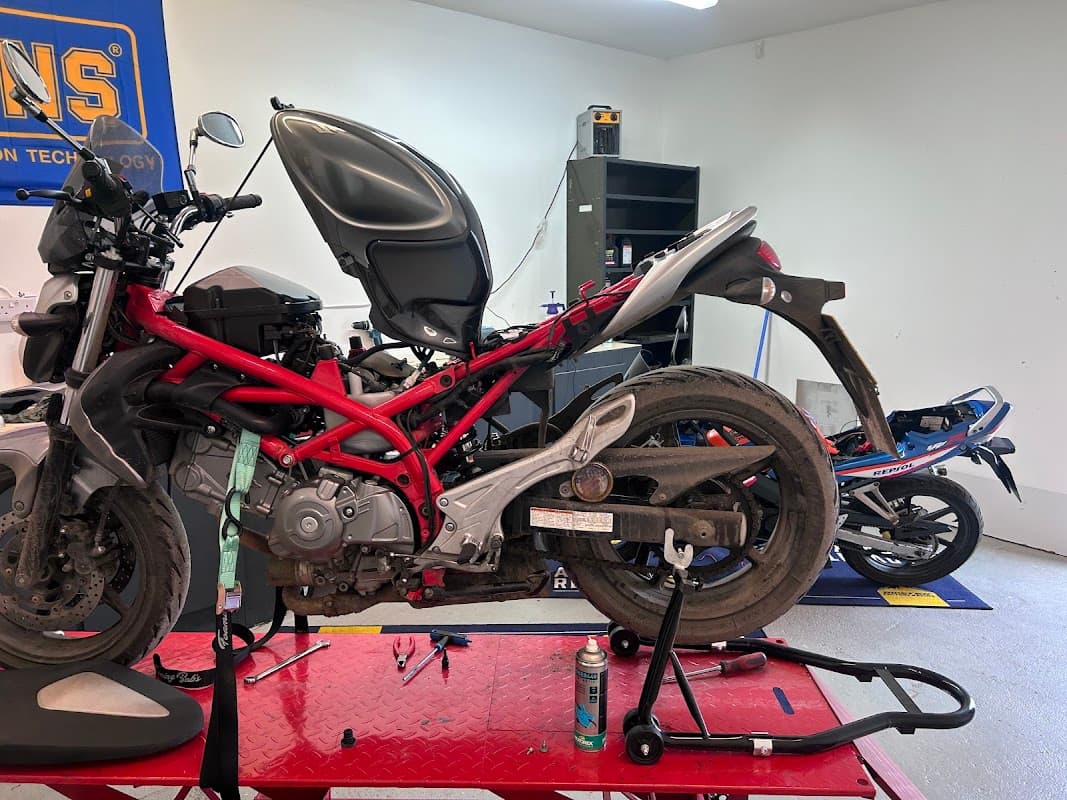 Motorcycles on a repair stand in a bike shop, tools and equipment visible in a well-lit workshop setting.