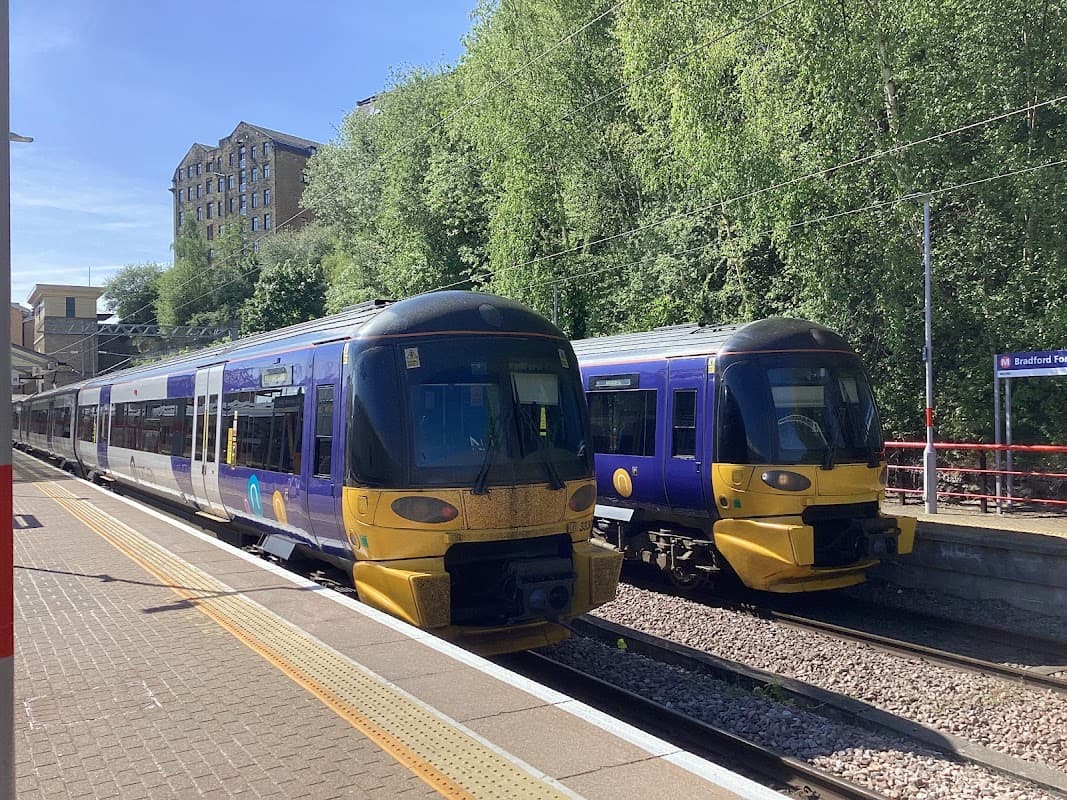Two trains at Bradford Forster Square station, surrounded by greenery and a clear blue sky.