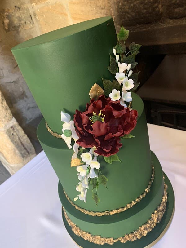 Three-tiered green cake adorned with a large burgundy flower, delicate white blossoms, and gold accents.