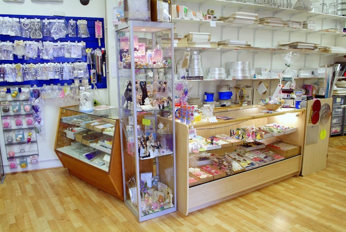 Brightly lit bakery shop interior with display cases filled with cake decorations and baking supplies on wooden flooring.