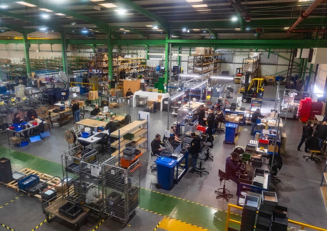 Interior of Debar Ltd ironmongery, featuring workers, shelves of materials, and organized workstations in a spacious warehouse.