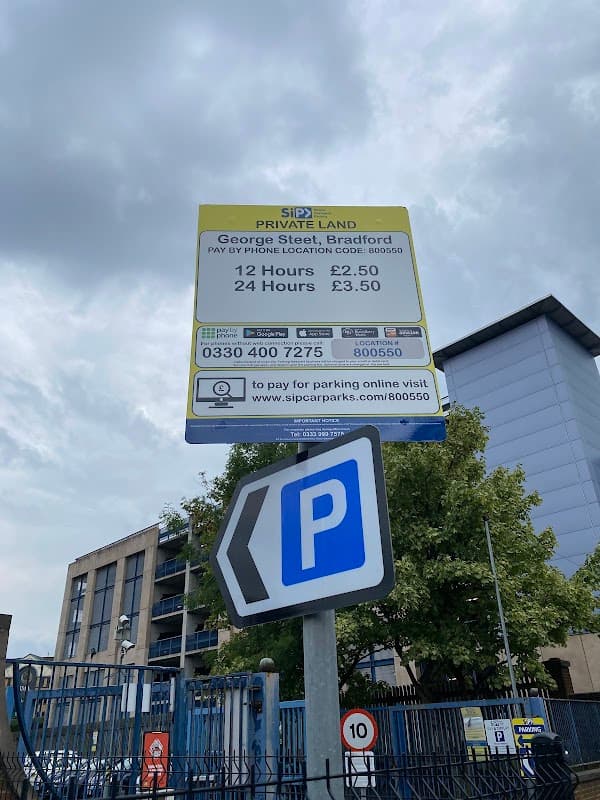 Sign for George Street Car Park with pricing details, phone number, and a parking symbol, surrounded by buildings and trees.