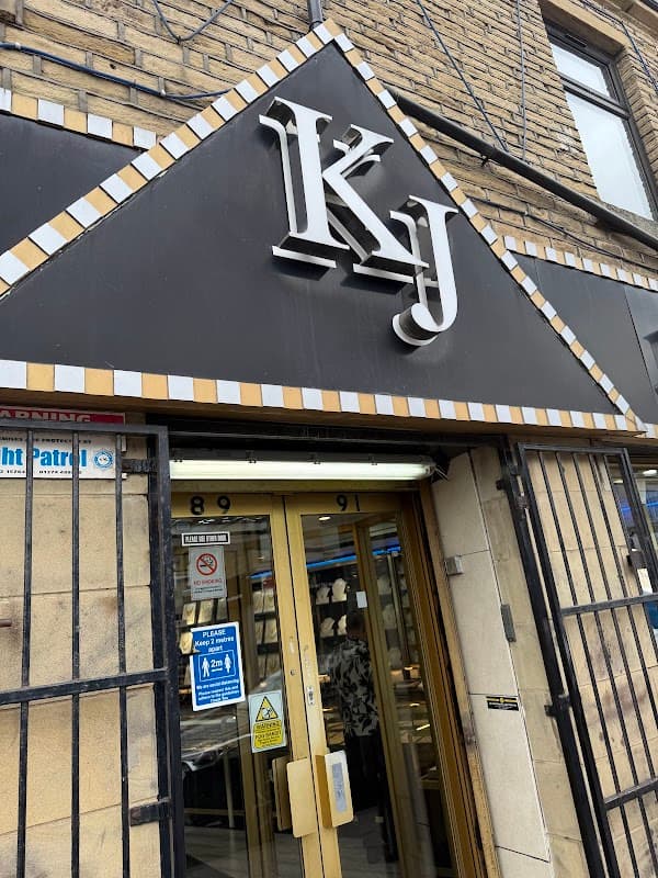 Sign for KJ Jewellers with a decorative black and gold facade, featuring a glass entrance and security bars.