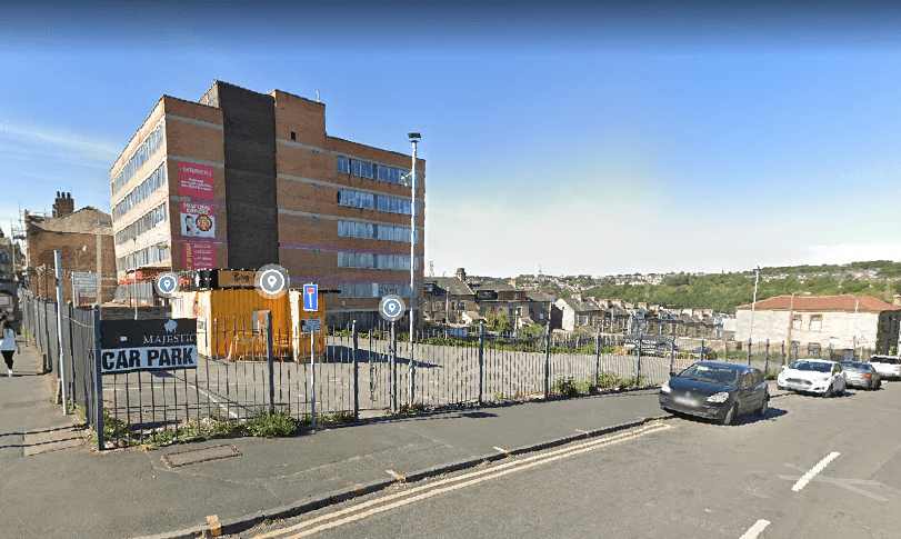 Majestic Hall Carpark with a fenced area, parked cars, and a multi-story building in the background under a clear sky.