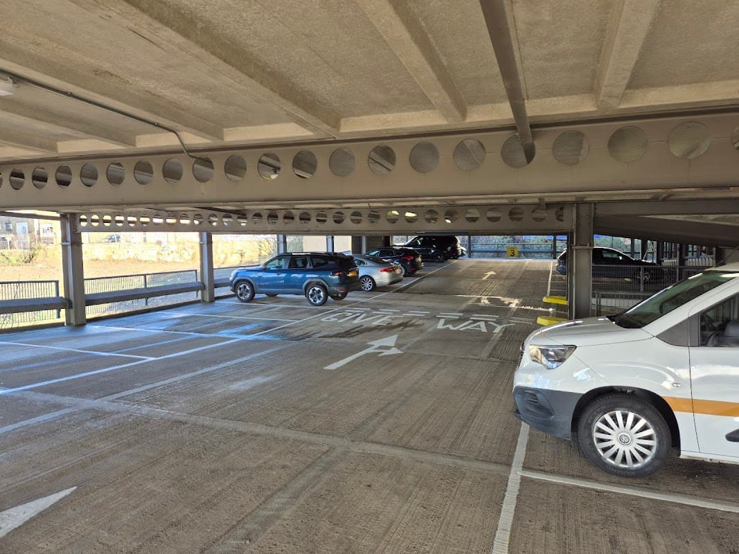 Multi-level car park with parked vehicles and a "Give Way" sign visible on the ground. Bright, open space.
