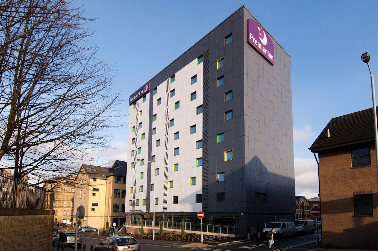 Modern multi-story hotel with a purple sign, surrounded by trees and vehicles in Bradford, Yorkshire.