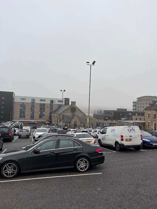 Car park filled with vehicles, including a black sedan and a white van, with buildings and fog in the background.