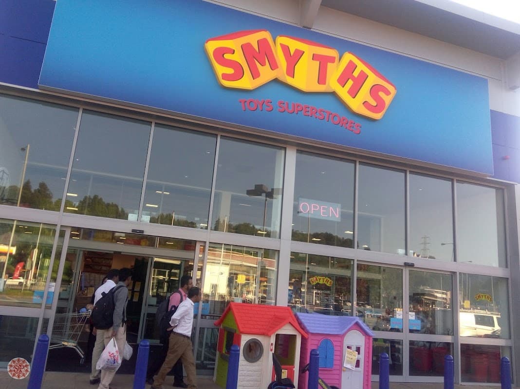 Brightly colored Smyths Toys Superstores sign above entrance, with open doors and a children's playhouse outside.