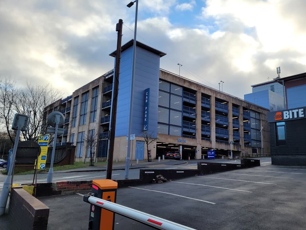 Multi-storey car park with blue and grey exterior, adjacent to a burger restaurant and parking barriers.