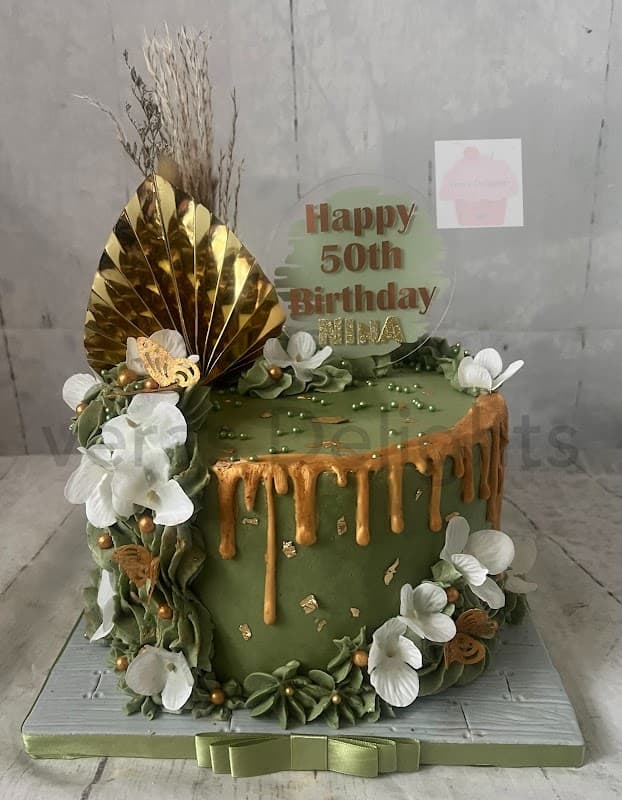 Green birthday cake with gold drip, white flowers, and a "Happy 50th Birthday" topper, adorned with decorative elements.