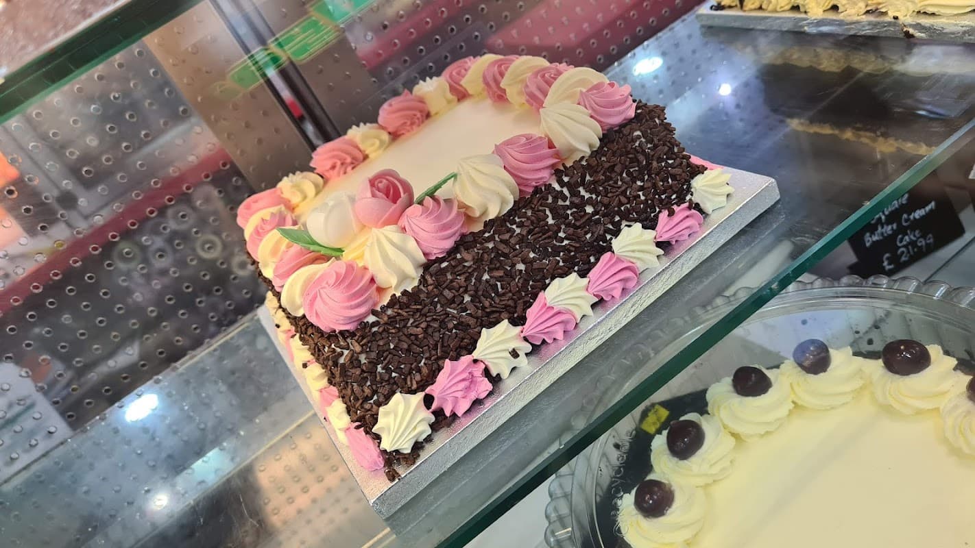 A beautifully decorated cake with pink and white frosting, topped with chocolate sprinkles and floral accents.