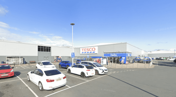 Car park outside a Tesco store in Bradford, featuring several parked cars and a clear blue sky.