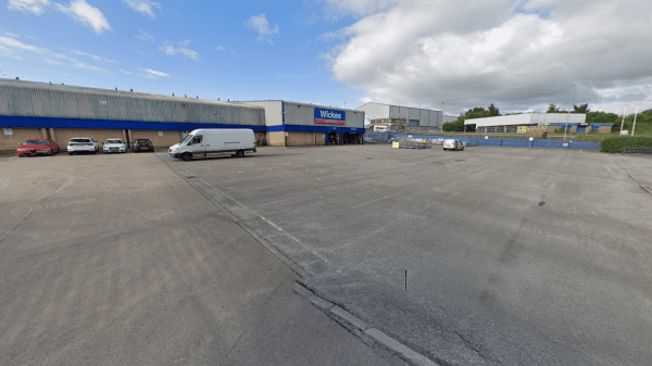 Empty car park with a van and a few cars, surrounded by industrial buildings under a partly cloudy sky.