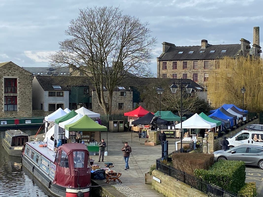 Colorful market tents line the waterfront, with a canal boat and historic buildings in the background.