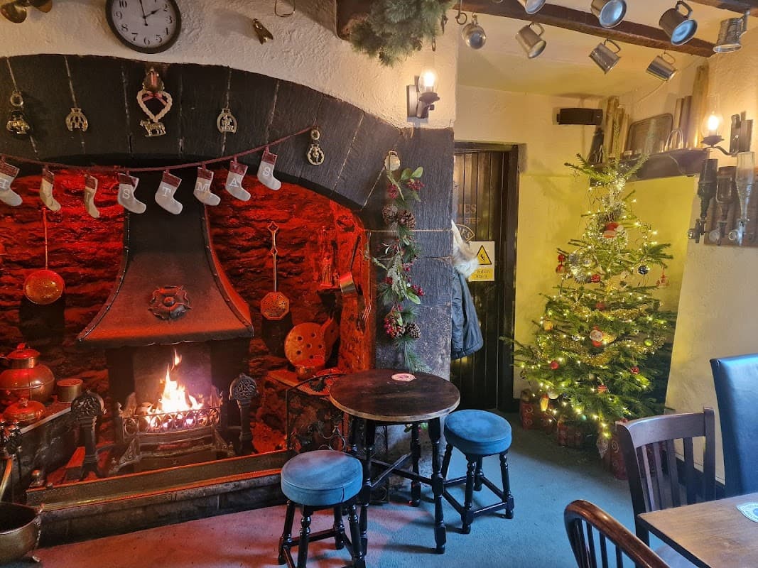 Cozy bar interior with a stone fireplace, festive decorations, a Christmas tree, and wooden tables and chairs.