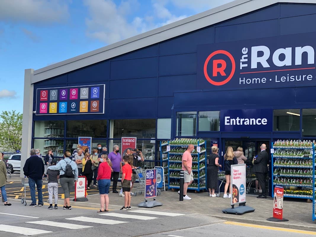 Crowd of people waiting outside The Range store in Bradley, North Yorkshire, with colorful signs and entrance visible.