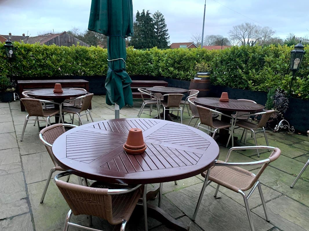 Outdoor seating area with round wooden tables and chairs, surrounded by greenery at The Oak Tree Inn.
