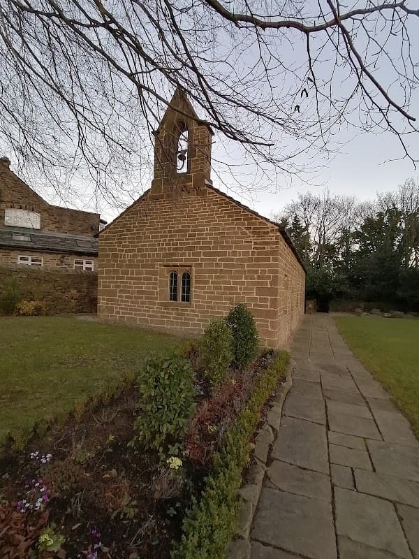Stone building with a bell tower, surrounded by greenery and a stone pathway, set in a tranquil outdoor area.