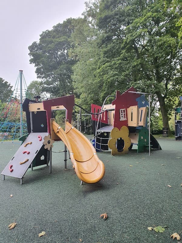 Colorful playground equipment with a slide, climbing structures, and surrounding trees in Bramhope, Yorkshire.