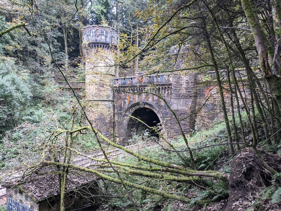 North portal of Bramhope Tunnel, featuring a stone archway and a tower, surrounded by lush greenery and fallen branches.