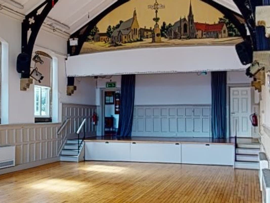 Spacious hall with wooden floor, large stage, and mural of Bramhope village on the ceiling.