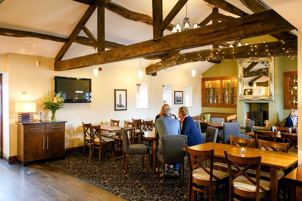 Cozy bar interior with wooden beams, tables, chairs, and a TV; patrons enjoying drinks in a warm atmosphere.
