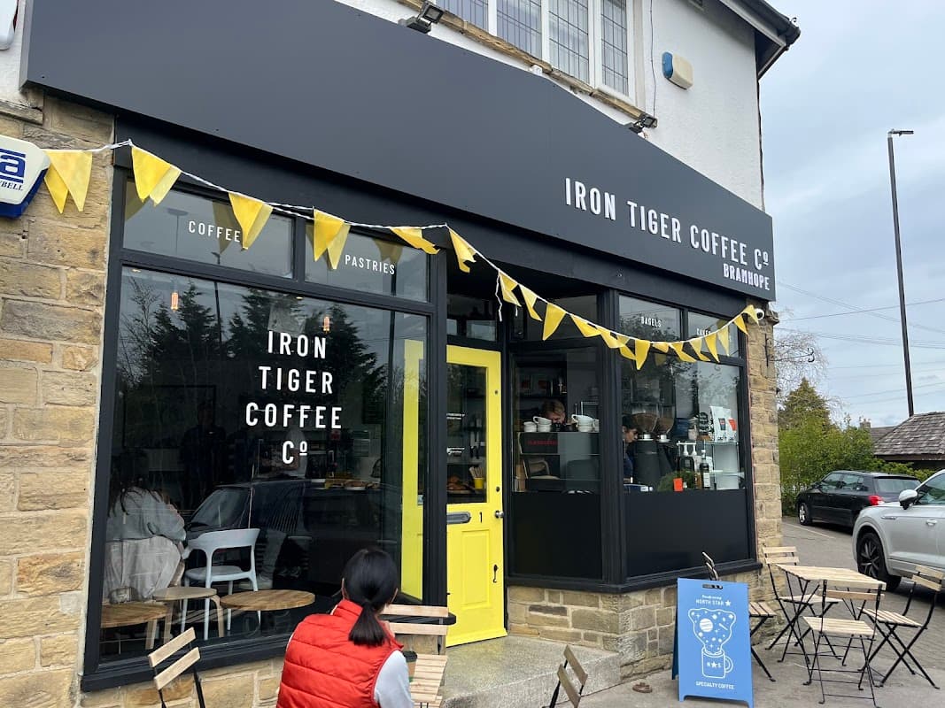 Black storefront with yellow accents, "Iron Tiger Coffee Co." sign, outdoor seating, and bunting in Bramhope, Yorkshire.