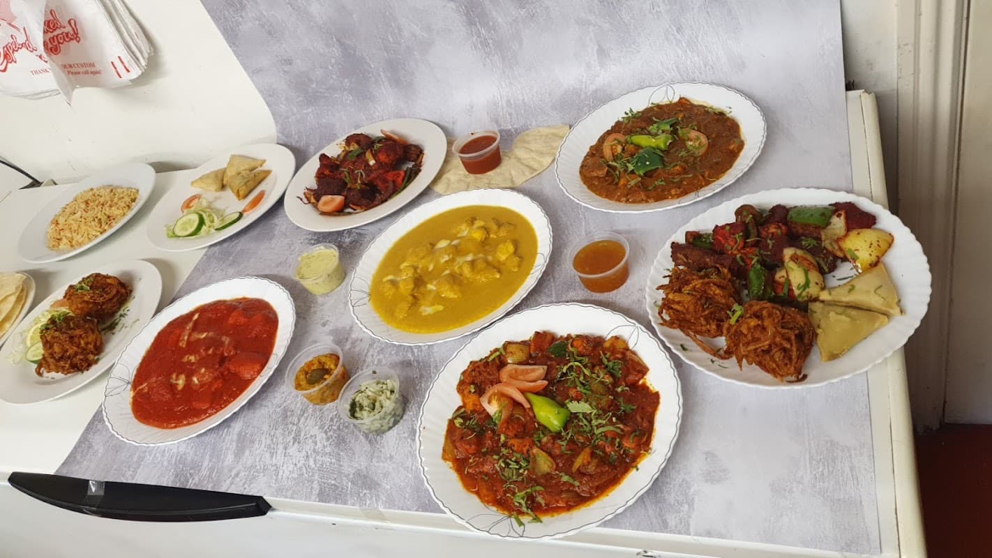 A variety of colorful dishes including curries, rice, and bread on white plates, arranged on a table.