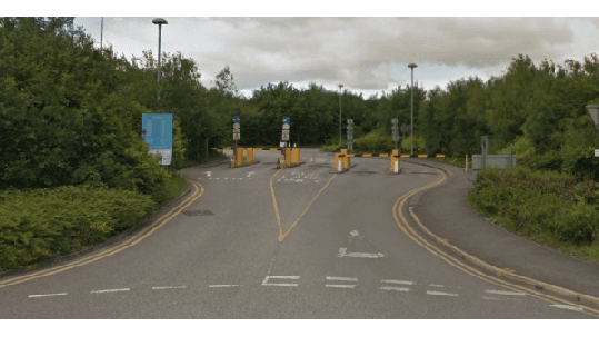 Entrance to a Pay & Display parking area with barriers, signs, and greenery in Bramhope, Yorkshire.