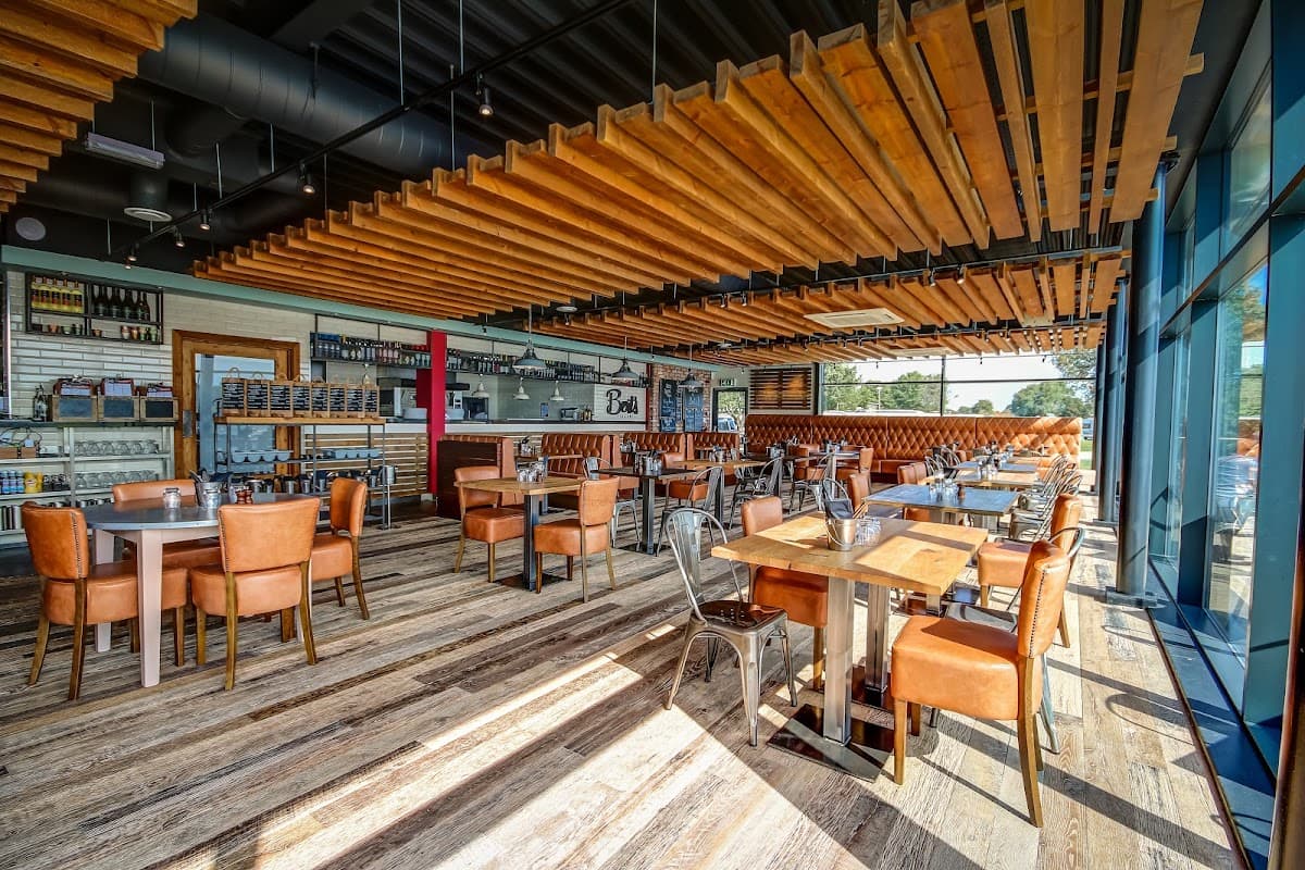 Bright, modern café interior with wooden beams, metal chairs, and tables, featuring a bar and large windows.