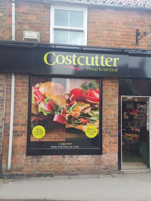 Costcutter storefront featuring fresh sandwiches and salads, with a brick wall background and colorful signage.