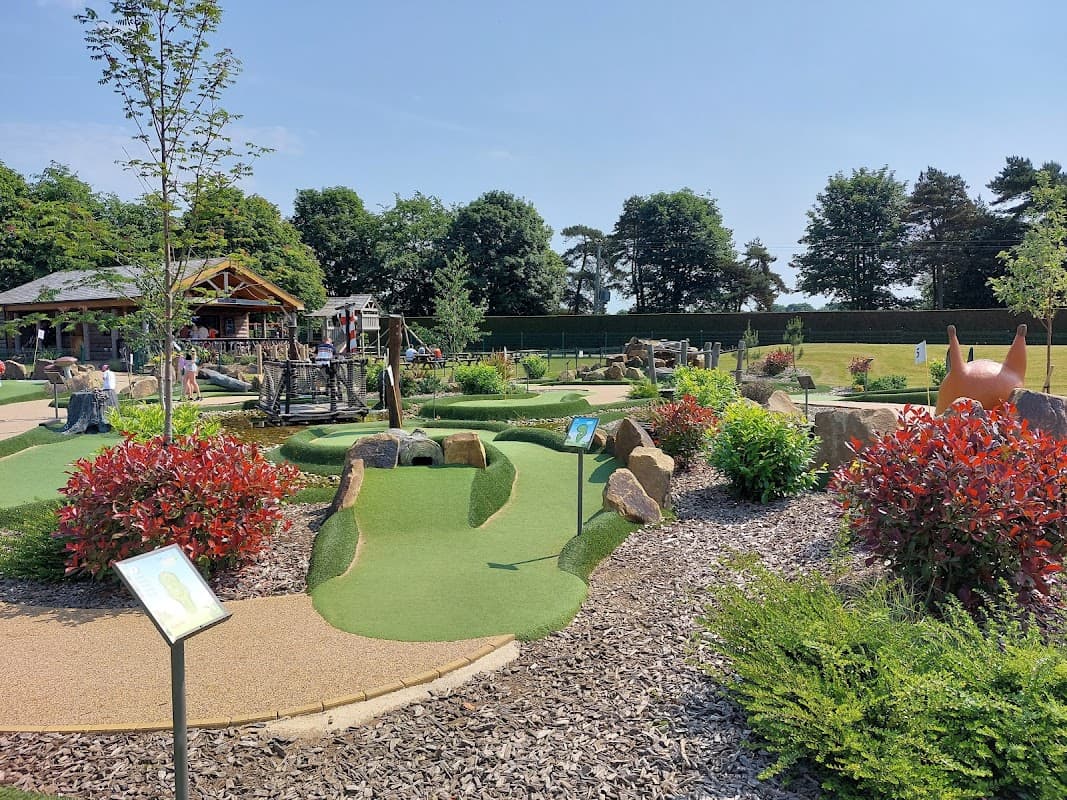 Mini golf course with vibrant greenery, playground equipment, and colorful shrubs under a clear blue sky.