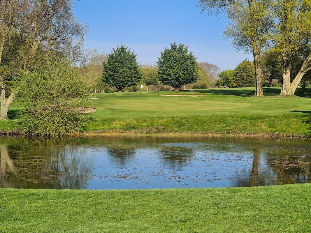 Lush green golf course with a pond, trees, and clear blue sky at Hainsworth Park Golf Club in Brandesburton.