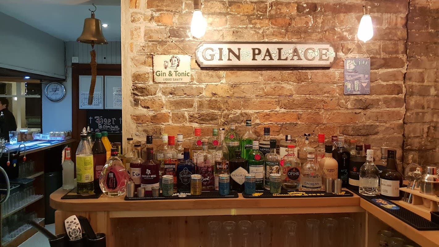 Bar counter featuring a variety of spirits, a "Gin Palace" sign, and a rustic brick wall backdrop.