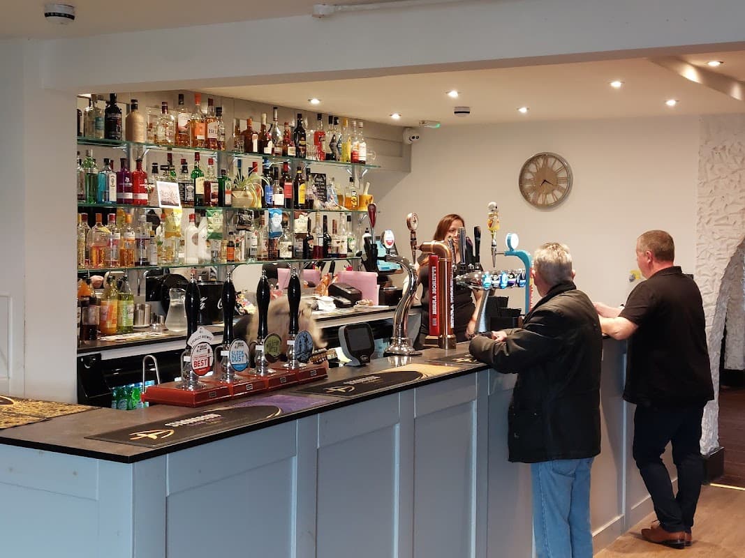 Bar area at The Dacre Arms featuring a variety of spirits, taps, and two patrons engaged in conversation.
