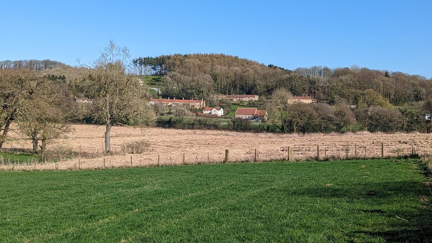 Cholmeley Hall nestled in a rural landscape, surrounded by fields and trees under a clear blue sky.