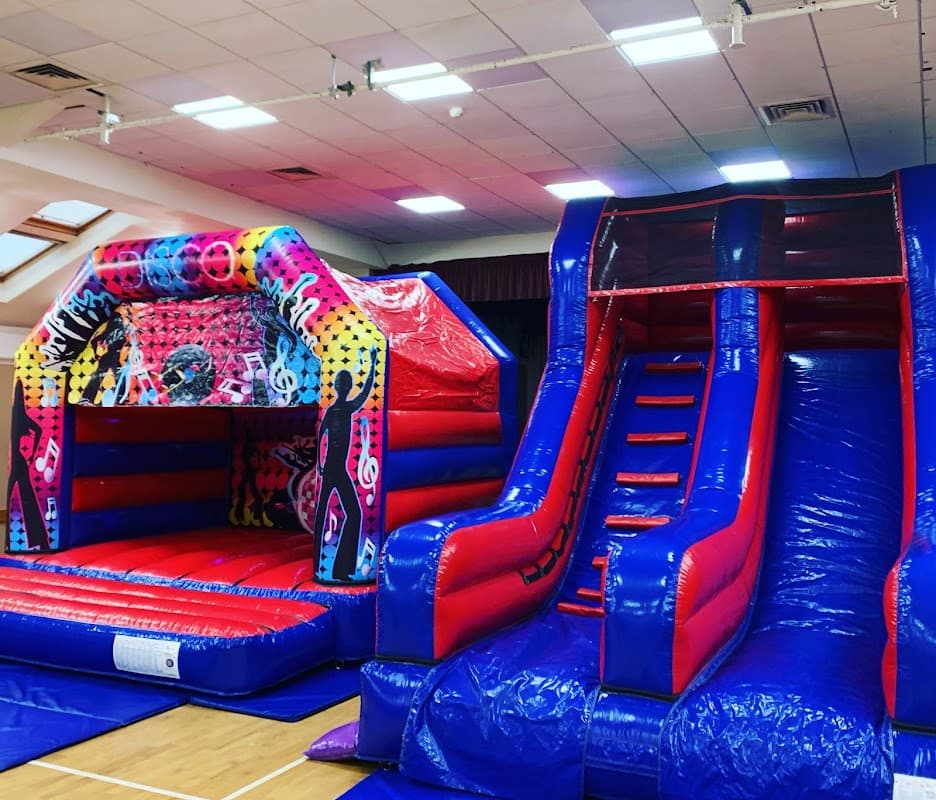 Colorful inflatable bouncy castle and slide in a spacious indoor hall with bright lighting.