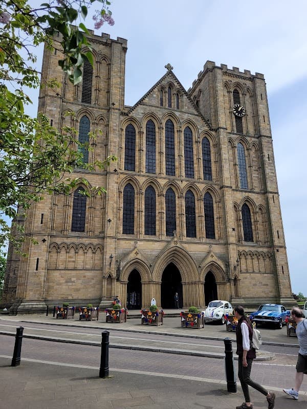 Historic stone hotel with large arched windows, clock tower, and decorative facade, surrounded by trees and pedestrians.
