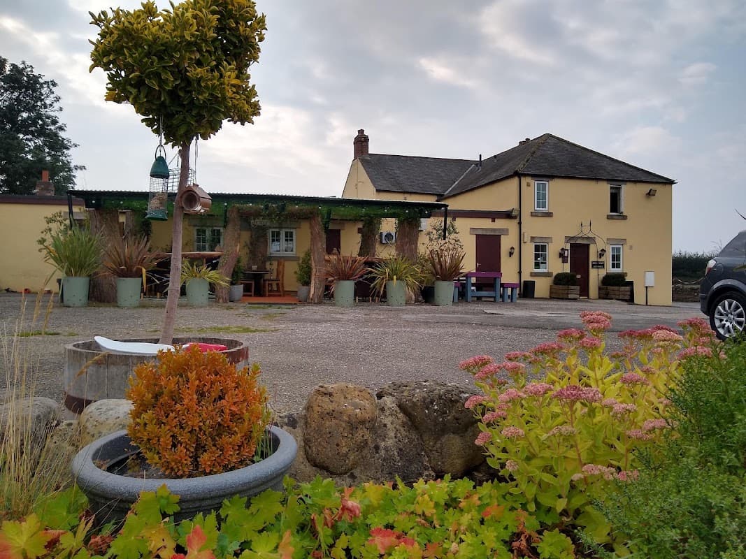 Yellow building of The Black-a-Moor Inn surrounded by greenery and colorful flowers, with a cloudy sky above.